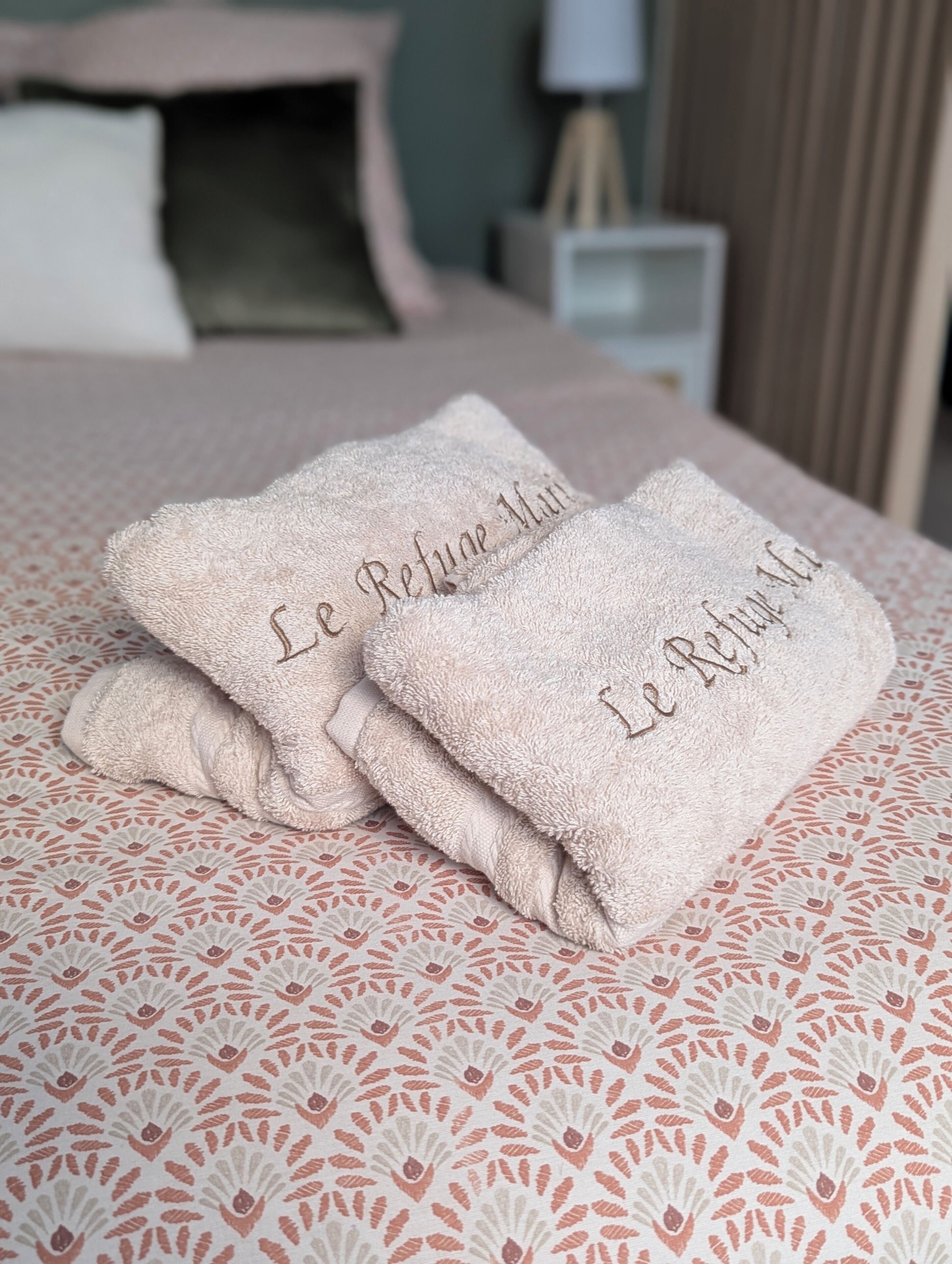Deux serviettes pliées, ornées de motifs brodés, sont posées sur un lit recouvert d’une couvre-lit à motifs.