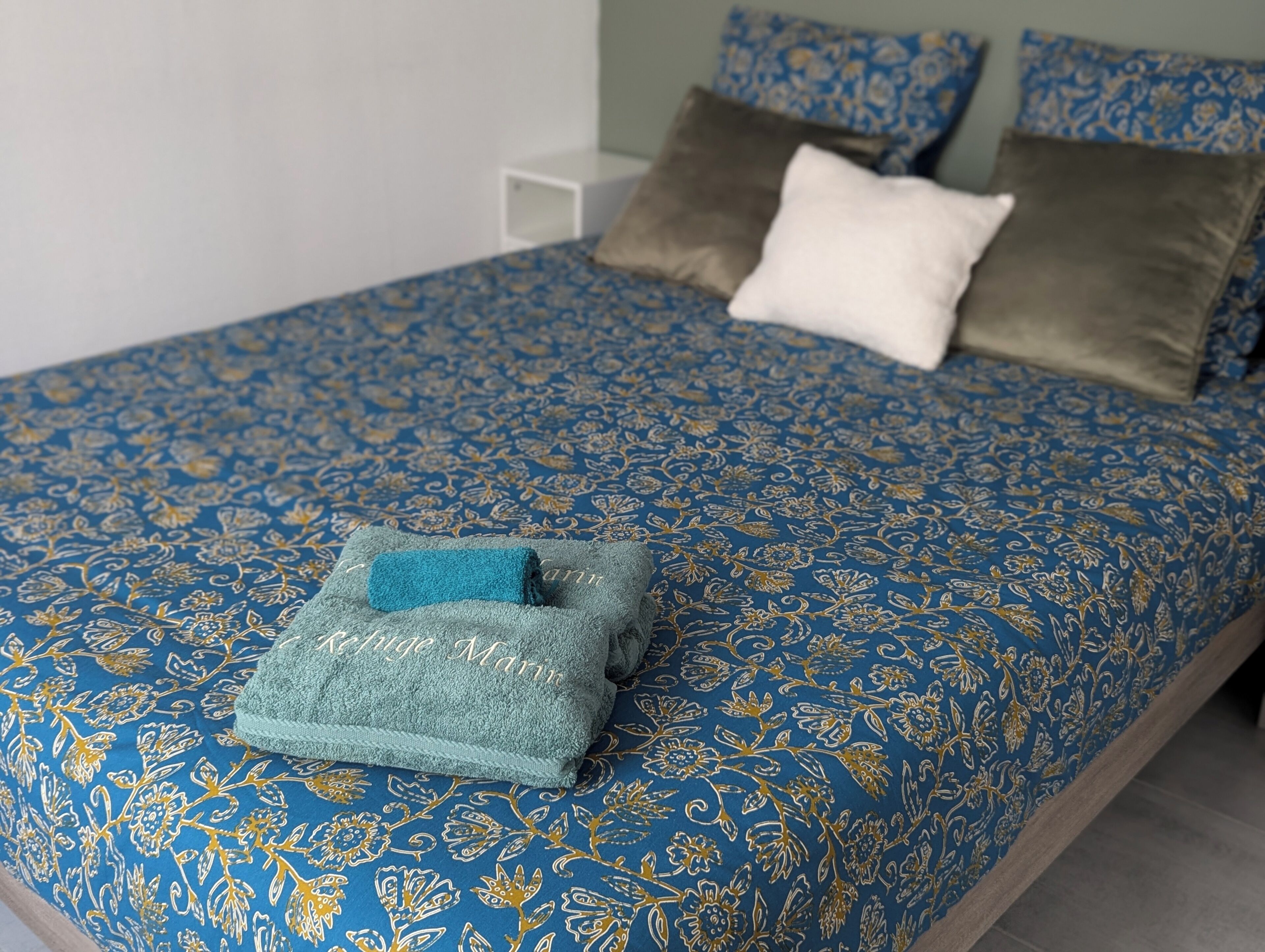 A bed with a blue floral bedspread, a white pillow, and a teal towel.