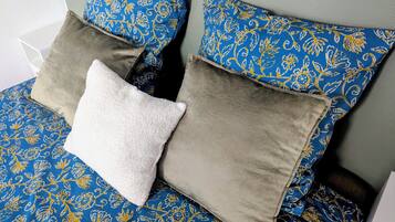 A bed with a blue floral bedspread, two pillows with a blue and gold pattern, and a white pillow.