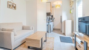A modern living room with a sofa, coffee table, and a kitchen area with appliances.