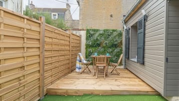 Une terrasse en bois avec une table et des chaises, entourée d’une clôture en bois et d’un mur végétal.