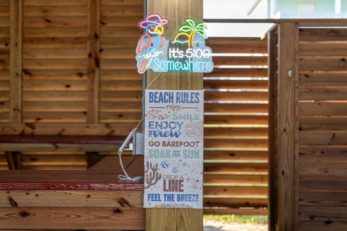 A wooden post with a neon sign and a list of beach rules.