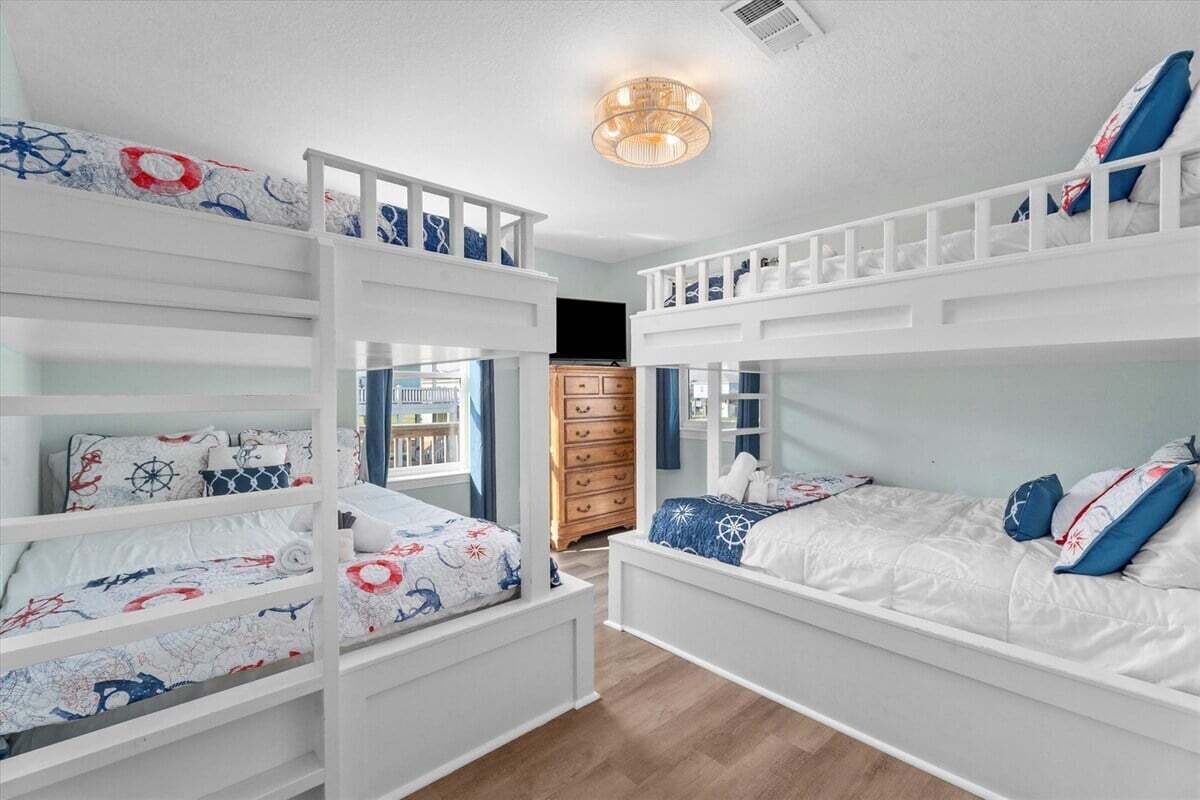A child’s bedroom with bunk beds, nautical-themed bedding, and a wooden dresser.