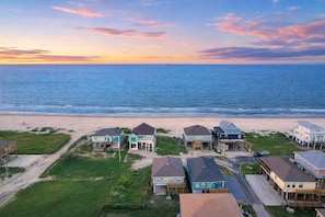 Uma área residencial costeira com casas perto da praia, apresentando uma vista clara do oceano e um céu ao pôr do sol.