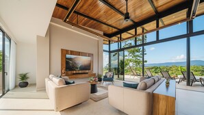 A modern living room with a large TV, comfortable seating, and a view of the outdoors.