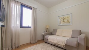 A living room with a sofa, a small table with a lamp, a framed picture on the wall, and a window with curtains. - Flat c Academia Sauna e Garagem - Jardim Paulista (São Paulo)