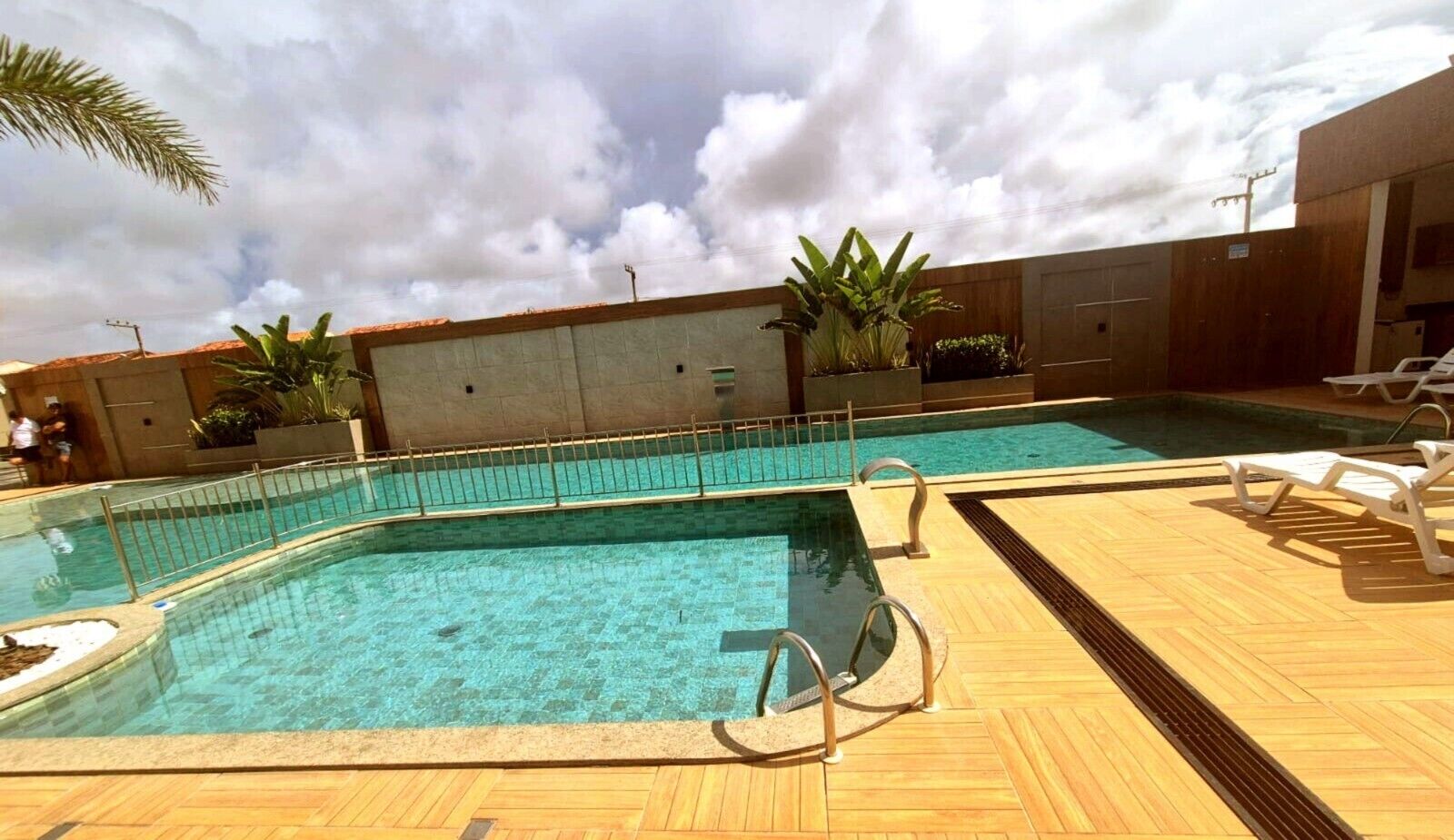 A rectangular outdoor swimming pool with a wooden deck, surrounded by a low metal fence.