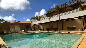 Una piscina con bordo piastrellato, circondata da lettini e un pergolato.