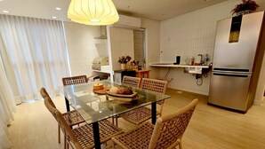 Una cucina moderna con un tavolo da pranzo in vetro, sedie in vimini, un frigorifero in acciaio inox e una lampada a sospensione.
