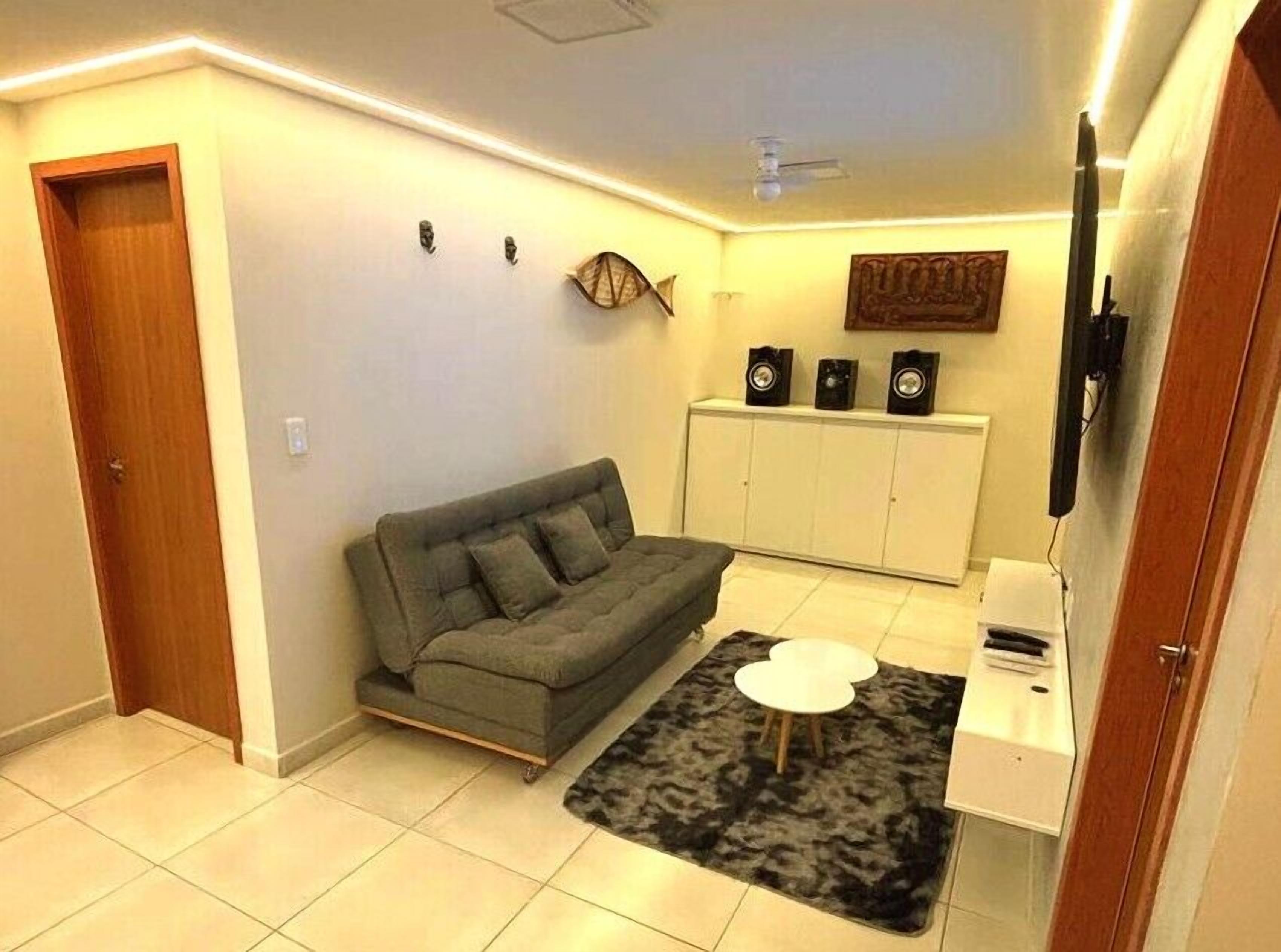 Ein Wohnzimmer mit einer Couch, einem kleinen weißen Tisch, einem Teppich, einem Schrank mit Lautsprechern und einem Fernseher.