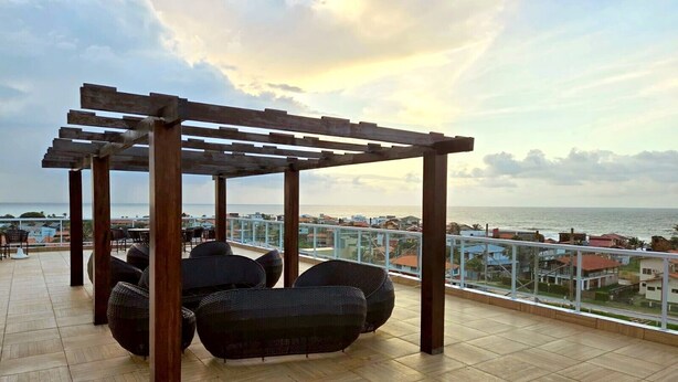 Una terrazza sul tetto con una pergola in legno, mobili in vimini e vista sul mare e sugli edifici.