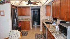 A kitchen with wooden cabinets, a refrigerator, a microwave, and a ceiling fan. - Beachfront condo at Mansions (TREASURE ISLAND)