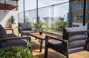 Ein moderner Außenbereich zum Sitzen mit Blick auf die Stadt, mit einem Holztisch, zwei grauen Sofas und einem Blumentopf.
