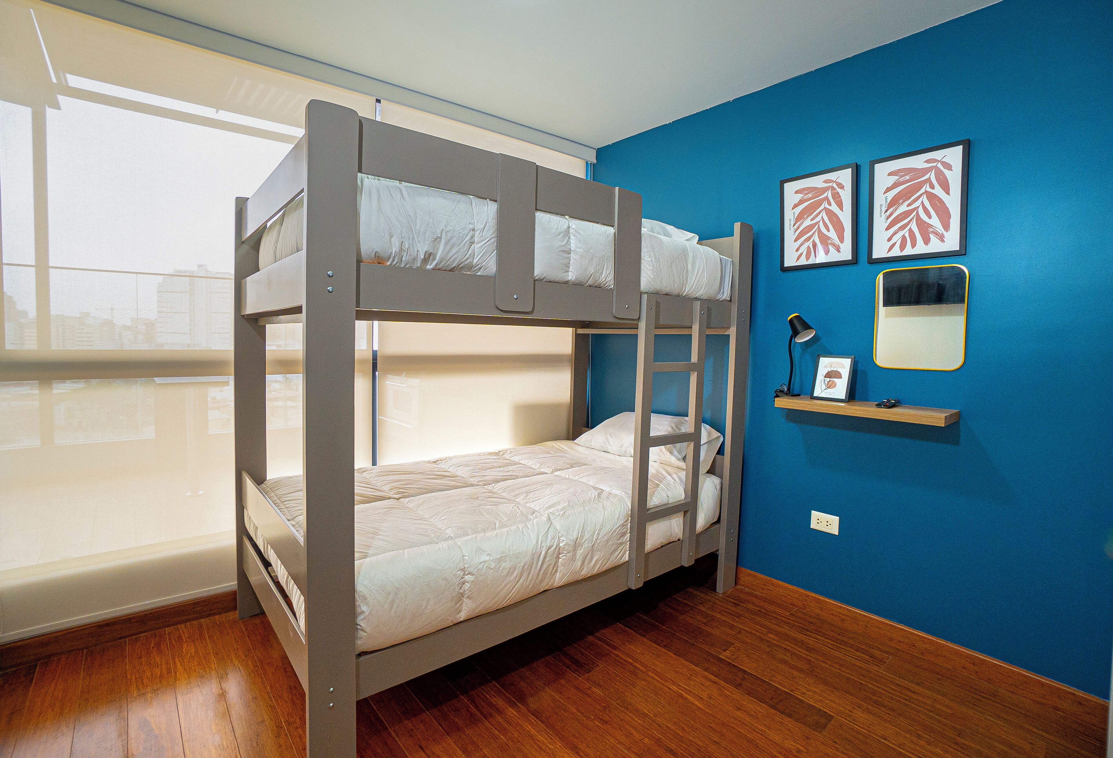 A bunk bed room with a window, a desk, and two framed pictures on the wall.