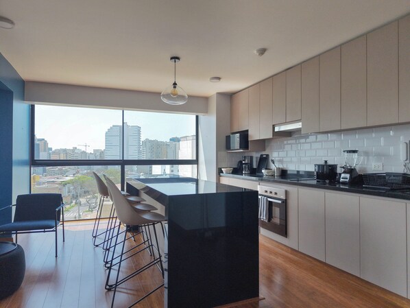 A modern kitchen with a large window, a dining area with chairs, and a view of the cityscape. - Spacious & Modern Duplex in Miraflores (Lima)