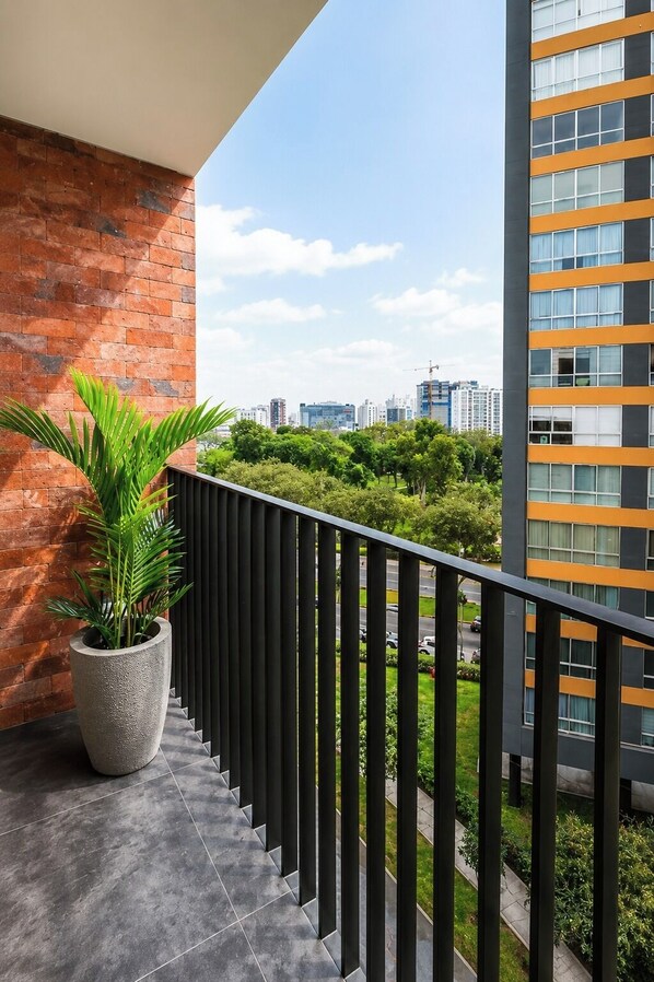 Ein Balkon mit einem Blumentopf, einer Ziegelwand und Blick auf eine Stadtlandschaft mit modernen Gebäuden.