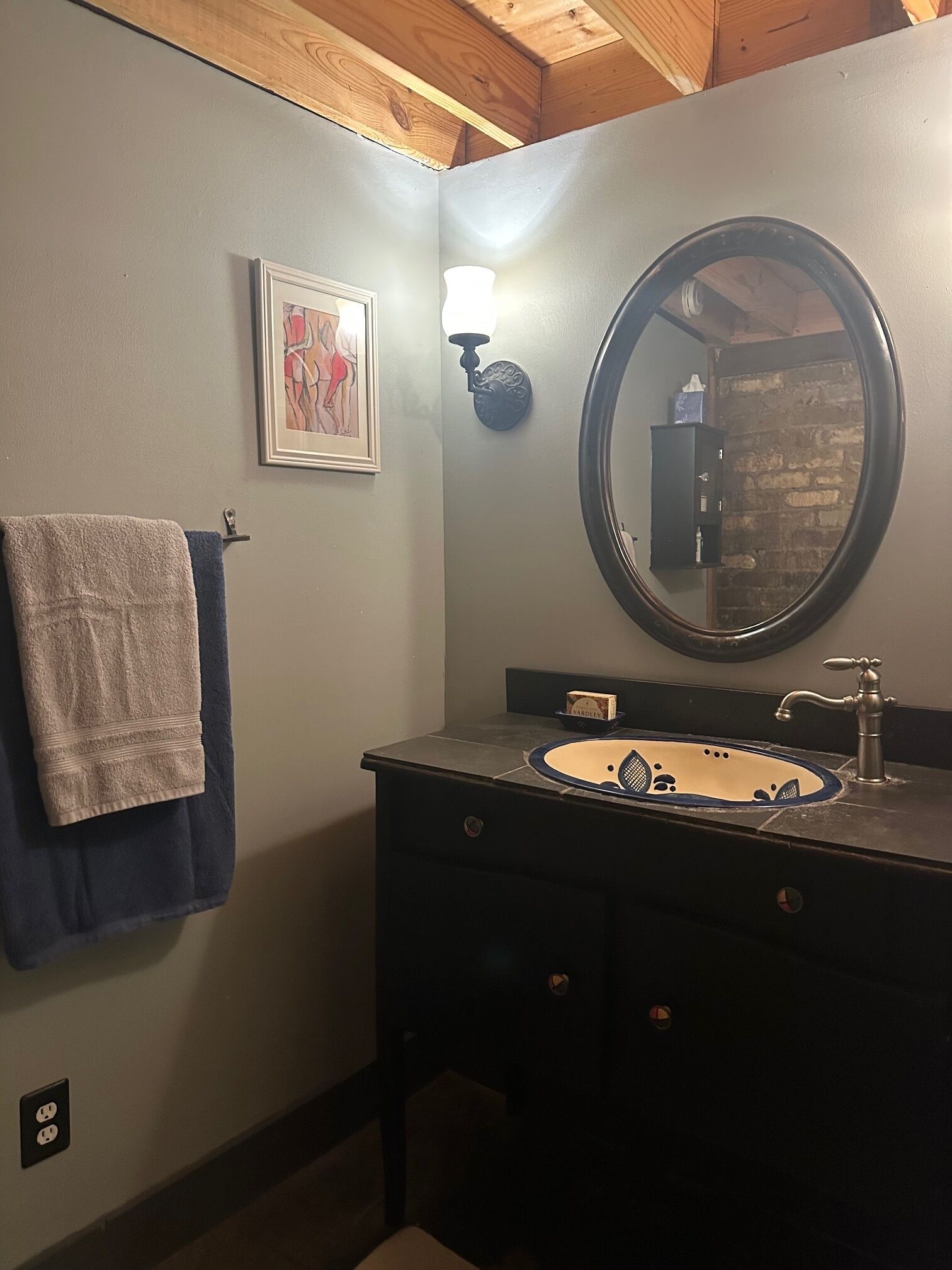 Een badkamer met een wastafel, spiegel, handdoekhouder en een kunstwerk in een lijst aan de muur.