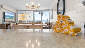 A modern kitchen with a marble countertop, a dining area with wooden furniture, and a large window offering a view of the sea. - Golden Arms 602 (New Smyrna Beach)