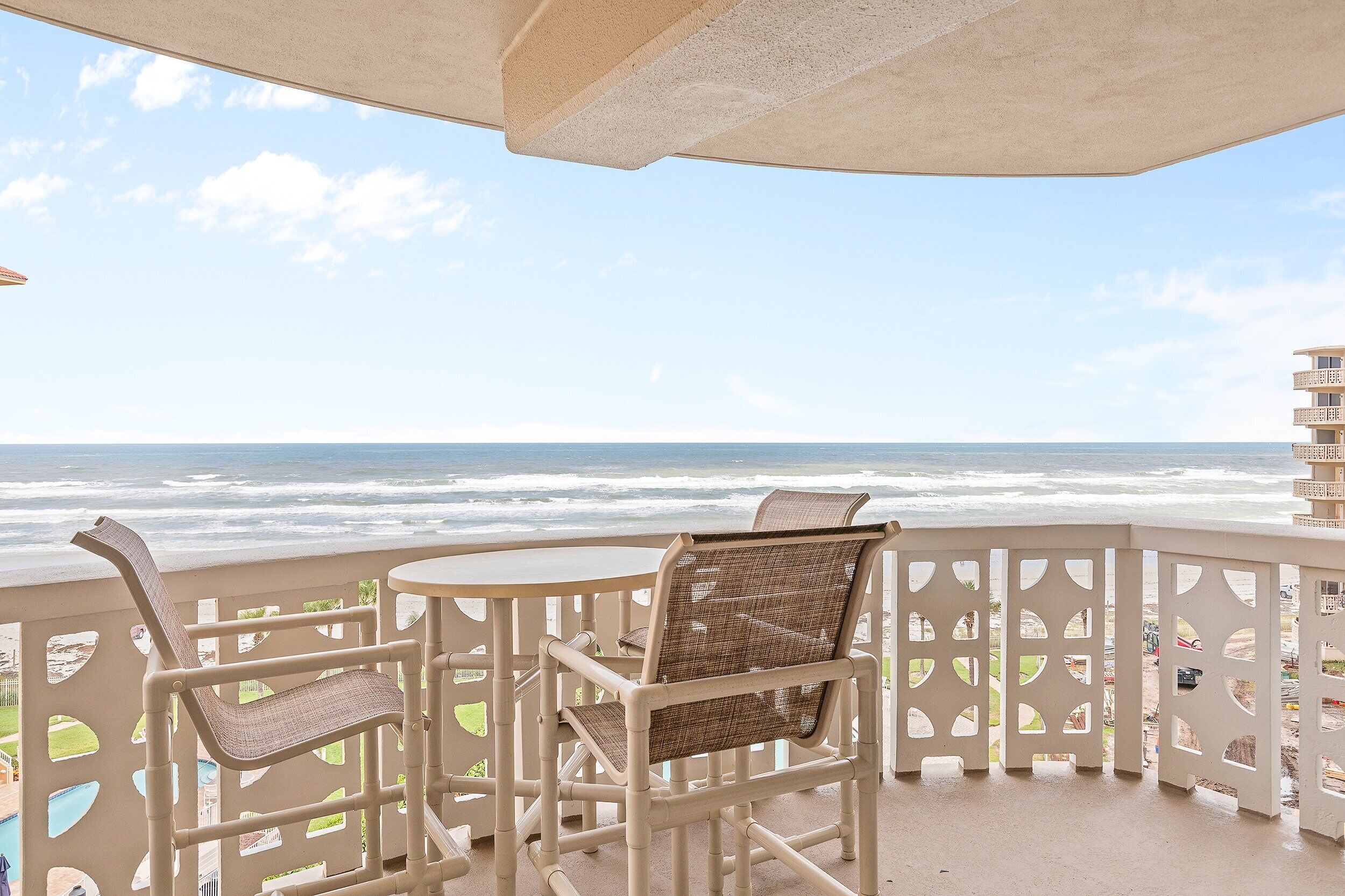 A balcony with a view of the ocean, featuring two wicker chairs and a small table.