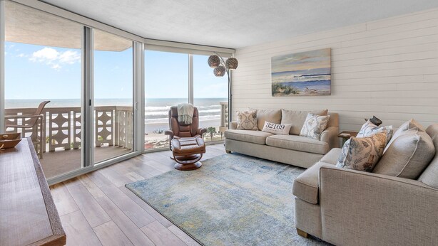A spacious living area with a large sliding glass door leading to a balcony overlooking the beach. - Golden Arms 602 (New Smyrna Beach)