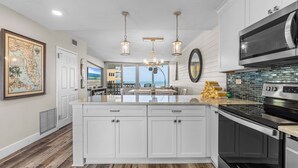 A modern kitchen with white cabinetry, a large island, stainless steel appliances, and pendant lighting. - Golden Arms 602 (New Smyrna Beach)