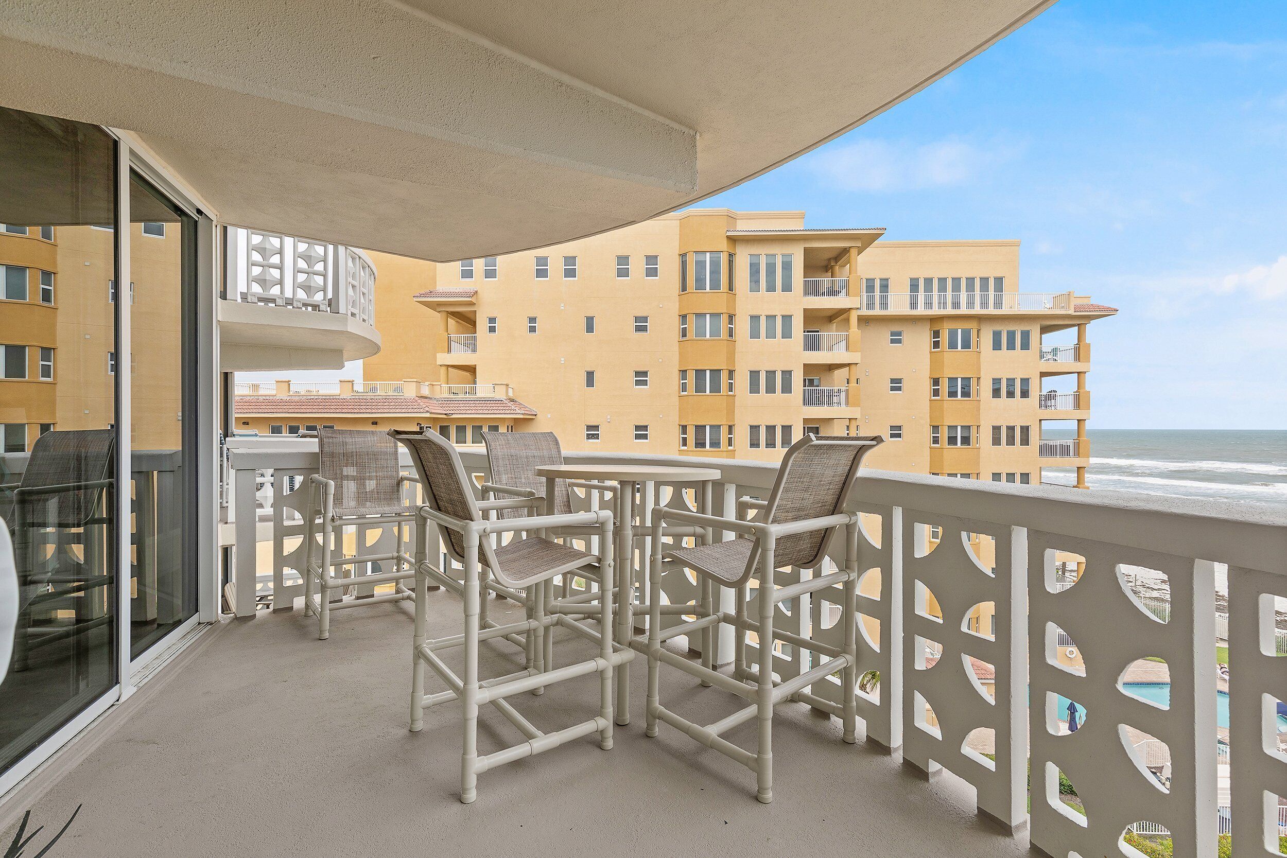 Un balcon agrémenté de mobilier d’extérieur, une vue sur l’océan et, au loin, un immeuble doté de balcons.