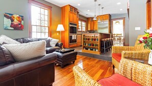 A spacious living room with a leather sofa, a wicker chair, and a dining area with wooden cabinets and a kitchen in the background. - New Listing! Grand Getaway w/ Pool & Hot Tub (Douglas)