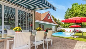 A covered outdoor dining area with a glass table and white wicker chairs, a swimming pool, and red umbrellas. - New Listing! Grand Getaway w/ Pool & Hot Tub (Douglas)