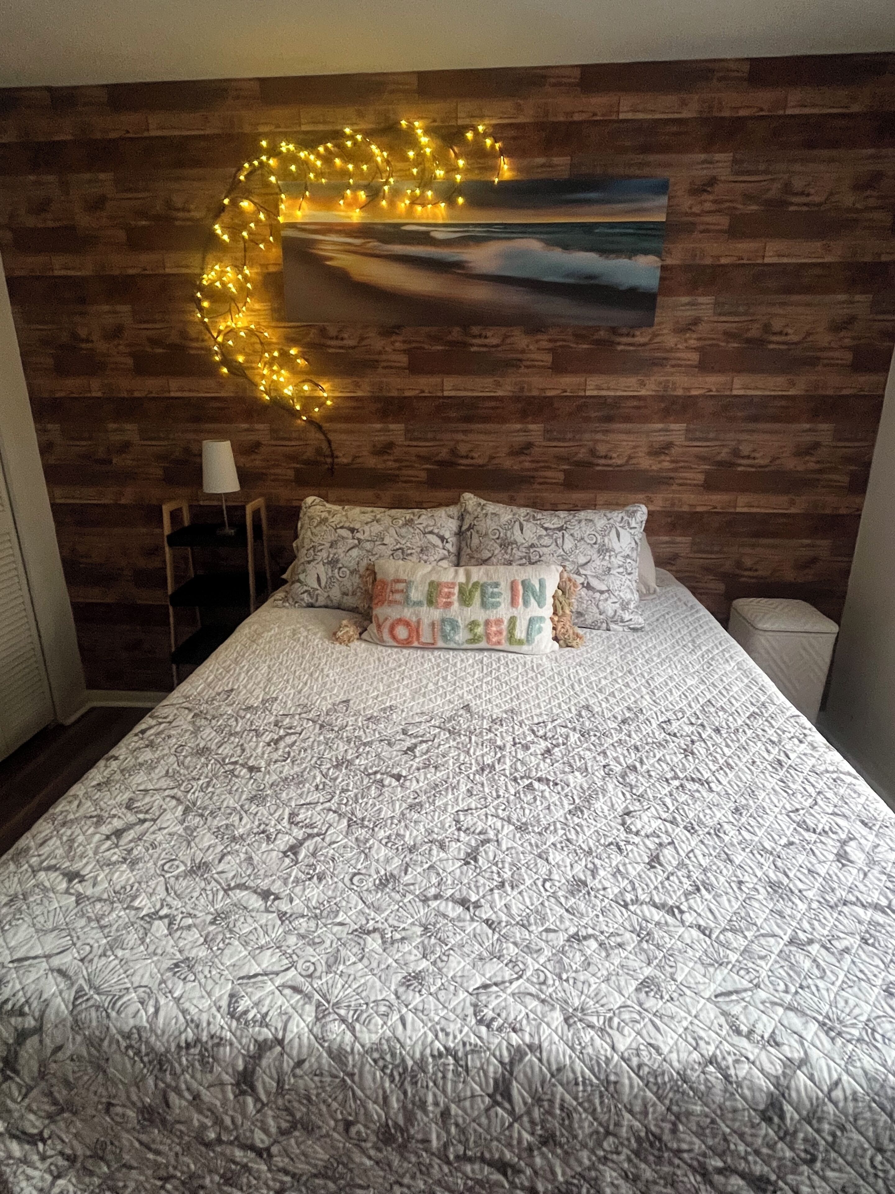 Une chambre à coucher avec une tête de lit en bois, un lit recouvert d’une literie à motifs et un tableau accroché au mur.