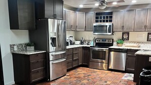 A kitchen with a brick floor, stainless steel appliances, and wooden cabinets. - Refuge Home, Jacuzzi & Heated Pool 35 min Orlando. (Eustis)