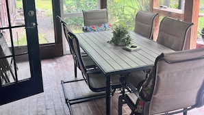 An outdoor dining area with a table and chairs, surrounded by large windows offering a view of lush greenery. - Refuge Home, Jacuzzi & Heated Pool 35 min Orlando. (Eustis)