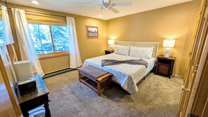 A bedroom with a bed, bedside lamps, a window with curtains, a bench, and a ceiling fan.