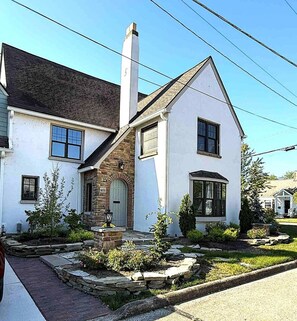 Una casa de dos pisos con fachada de piedra, una chimenea y un porche delantero con un pequeño jardín.