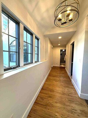 Un pasillo con amplios ventanales, suelo de madera y una lámpara moderna.