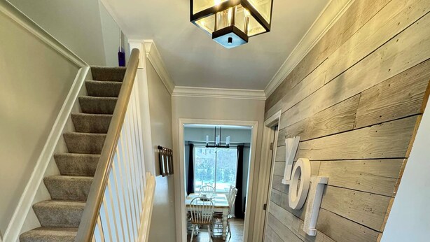 Un couloir avec un plancher en bois, un escalier doté d’une rampe blanche, et un coin repas à l’arrière-plan.