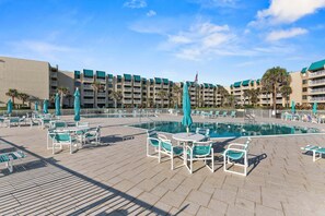 Un espace piscine d’hôtel avec plusieurs chaises longues et parasols, une piscine et un bâtiment avec des balcons en arrière-plan.