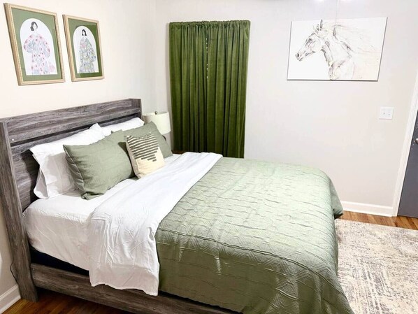 Une chambre à coucher avec un lit, des rideaux verts, un mur blanc et deux tableaux encadrés.
