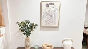 A wooden cabinet with two doors, a vase with green foliage, a small blue candle, and a white ceramic jug on top. - Katie Mae’s Downtown Retreat (Atlanta)