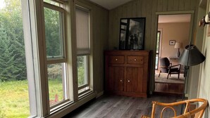 Une pièce dotée de grandes fenêtres, d’un plancher en bois, d’une table à manger avec des chaises, d’une armoire et d’un luminaire au plafond.