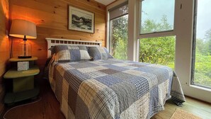 Une chambre confortable avec un grand lit, une table de chevet, une lampe et une fenêtre donnant sur un paysage verdoyant.