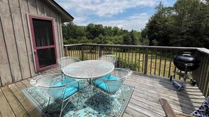 Une terrasse en bois avec une table et des chaises, un barbecue et une porte.