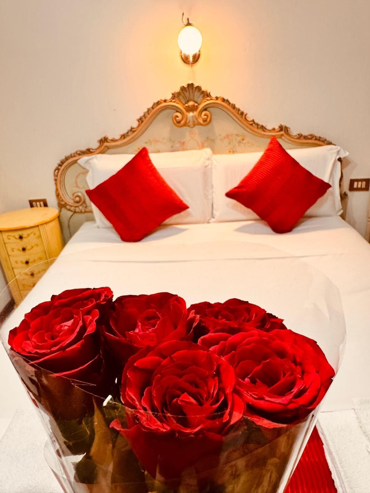 A bed with ornate headboard, white linens, and red pillows.