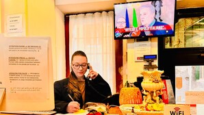 A hotel reception desk with a TV displaying a news channel, a WiFi sign, and a decorative centerpiece. - HOTEL HENRY (Venice)