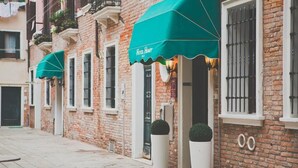 A row of brick buildings with green awnings, a visible entrance, and potted plants. - HOTEL HENRY (Venice)