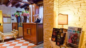 A reception area with a checkered floor, wooden reception desk, and a stone wall. There are posters and a lamp on a table. - HOTEL HENRY (Venice)