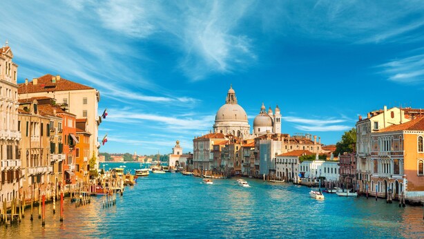A canal with boats, historic buildings, and a prominent dome structure. - HOTEL HENRY (Venice)