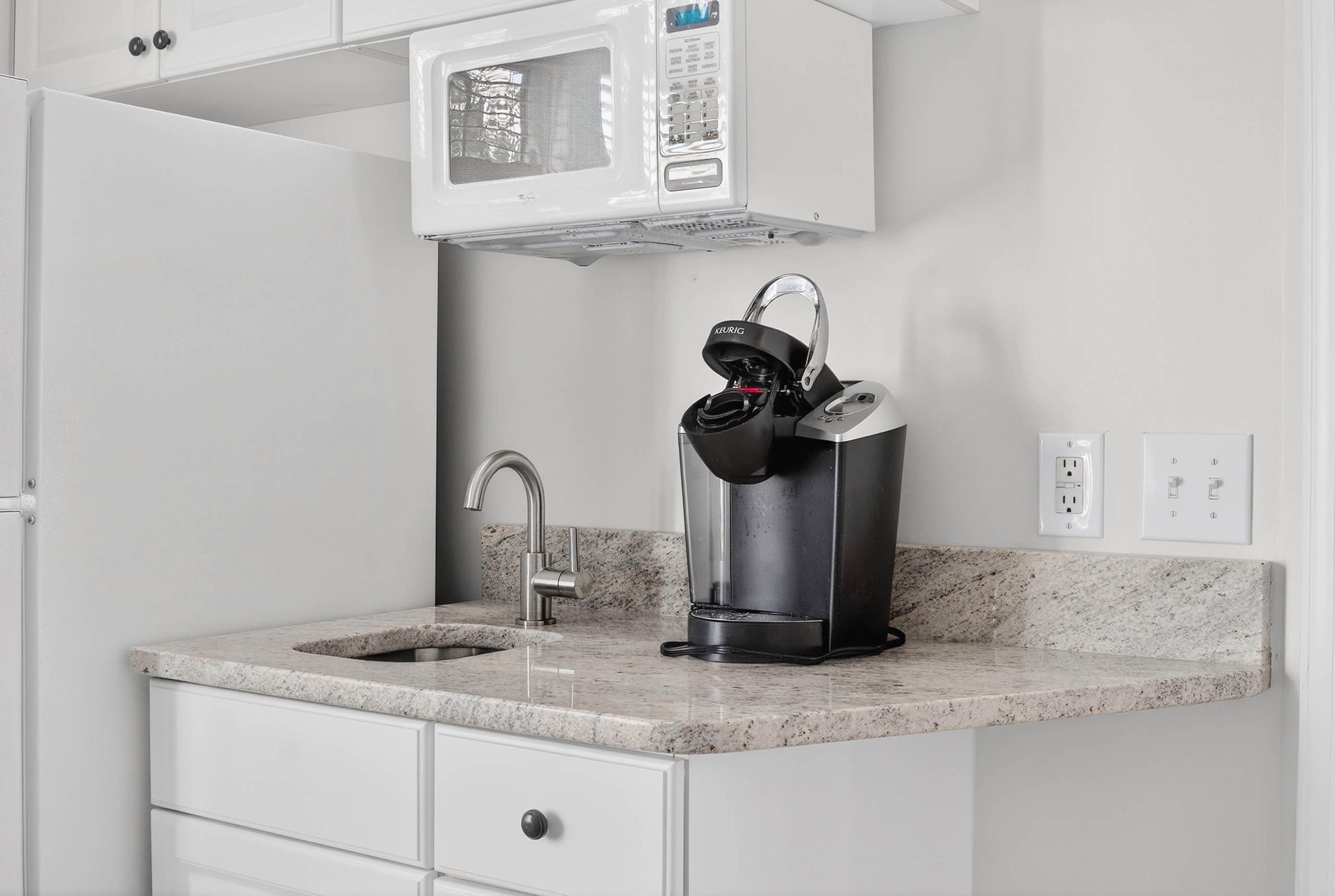 A kitchen with a built-in microwave, a coffee maker, a sink, and a marble countertop.