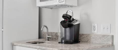 A kitchen with a built-in microwave, a coffee maker, a sink, and a marble countertop.