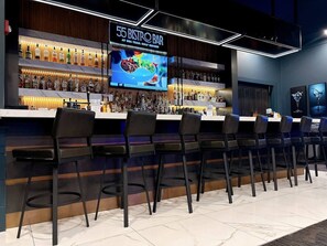 Un espace bar avec de nombreuses bouteilles d’alcool, un écran affichant le menu et des tabourets de bar.