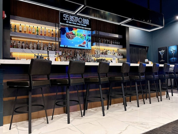 Una zona de bar con varias botellas de licor, un menú digital y taburetes.